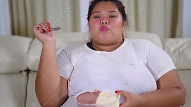 Overweight woman enjoying ice cream on sofa