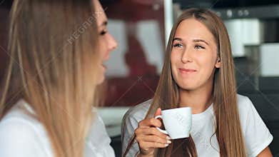 Two women friends in a kitchen drinking coffee, talking and having fun