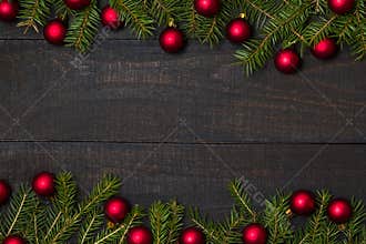 Dark rustic wood table flatlay - Christmas background with red ball ornament decoration and fir branch frame. Top view with free