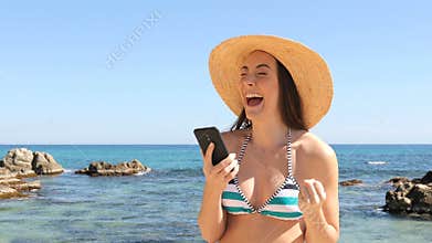 Excited woman in bikini reading good news on phone