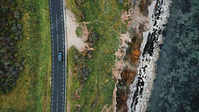 Top view, drone zooms in tracking black SUV car driving on autumn road trip near beautiful eroded sea shore coastline.