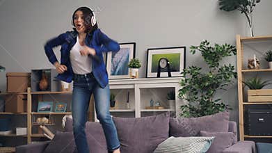 Joyful woman singing and dancing listening to music in headphones at home