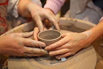 Hands of two people create pot on potter's wheel