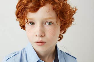 Close up portrait of funny little kid with orange hair and freckles. Boy looking in camera with relaxed and calm face