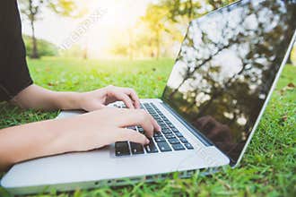 Young asian woman legs on the green grass with open laptop. Girl hands on keyboard. Distance learning concept.