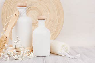 Soft elegant bathroom decor of white cosmetics bottles with comb, flowers on white wood board, mock up, copy space.