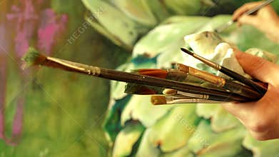 Professional artist painter holding brushes in her hand drawing an artwork with oil paints