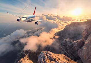 Landscape with white passenger airplane, mountains, sea and orange sky