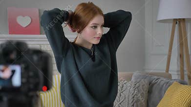 Young red-haired girl blogger, smiling, talking at the camera, Makes herself a hairstyle, tress, home comfort in the