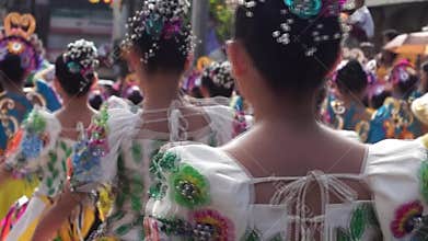 Backside close up of cultural dancers in various coconut costume dance along the streets to celebrate patron saint.