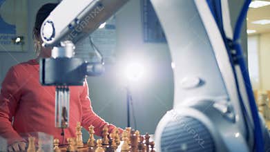 A little dark haired girl is playing chess with a robotic arm