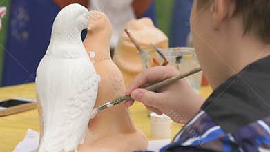 Child painting brushes on the clay figure outdoors