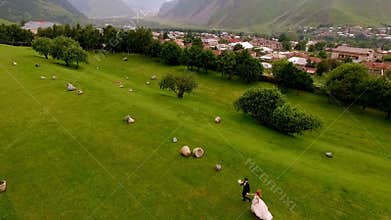 Wedding. The bride and groom are run along the green grass against the backdrop of the mountains