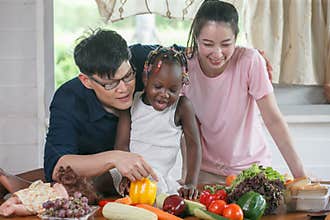 Asian couple cooking and tasting food with african american girl together in kitchen at  home