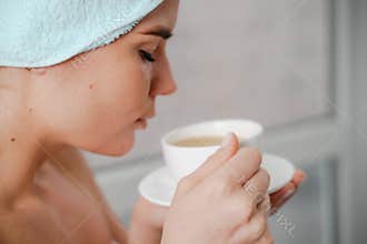 Young serene relaxed woman in spa bath towel drinking hot beverage tea coffee after taking shower bath at home. Beauty