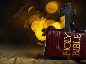 On a wooden table there is a Holy Bible and a Catholic cross on a bright yellow background. There are no people in the photo.