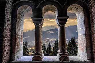 Beautiful gothic medieval arched stone window. Magnificent majestic view from the window. Winter mountains and a castle