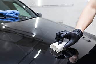 The process of applying a nano-ceramic coating on the car`s hood by a male worker with a sponge and special chemical composition