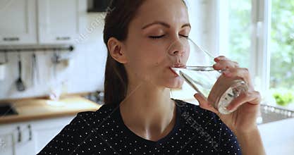 Young 20s european girl drinking pure stilled aqua in kitchen.