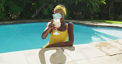 Portrait of happy african american woman standing in swimming pool making a toast with her drink