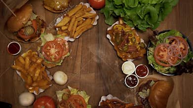 Serving burger on a table full of fast food meals. Top down overhead view of fried foods on a wooden table