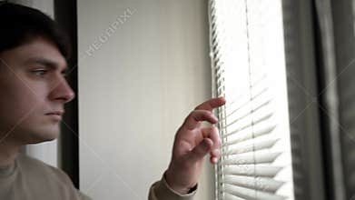 Anxious man looking out from blinds, handheld shot