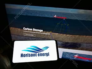 Person holding cellphone with logo of Norwegian carbontech company Horisont Energi AS on screen in front of business webpage.