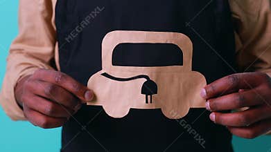 mixed race man holding paper car with recharging socket in blue studio background eco electro car concept