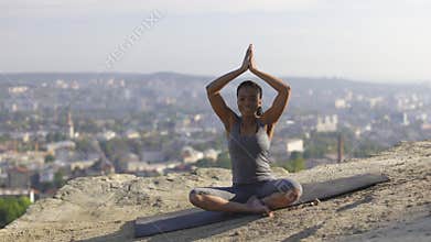 Sporty woman practicing yoga on mat on high hill