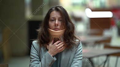 Adult woman with injured neck is wearing cervical collar and sitting in cafe alone, pain expression on face