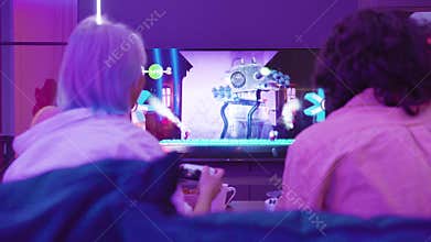Back view of young couple play video game Sackboy Little big Planet on a Xiaomi Mi TV using PlayStation 5 gaming console
