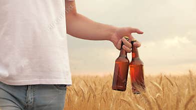 A man with two bottles of beer walks through a wheat field. farmer brewer carries fresh cold beer through a field of