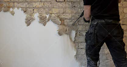 Worker removing plaster from indoor brick wall with sds drill
