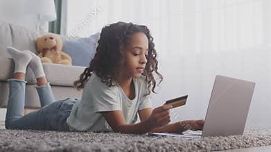 Little african american girl making online payment on laptop, enjoying successful transaction with banking app