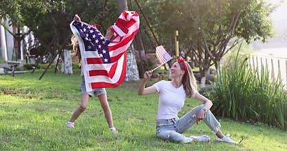 Cute Little Girl seven years old and young mother with blonde hair in casual clothing waving national USA flag outdoors