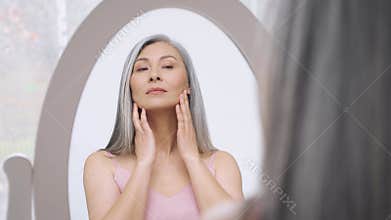 Gorgeous Asian mature woman looking at mirror. Perfect natural makeup.