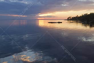 The soft gray, yellow and pink of the sunset sky over the lake with reflection
