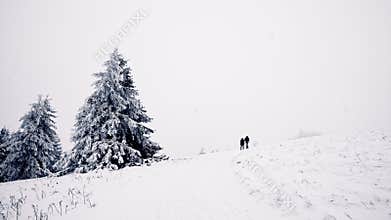 Two people hike up the mountain in deep snowy and misty winter landscape