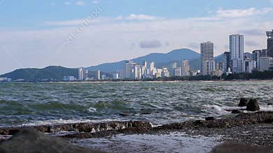 Surf overlooking city, calm waves, reinforced concrete fortifications on coastline.