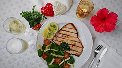 Grilled swordfish steak with fresh salad, tomatoes and cheese on a plate rotating. Valentines day. Pour champagne into a glass.