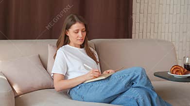 Video of young woman sitting on sofa and writing on agenda