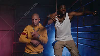 Cool funky rappers team gesturing and dancing together in dark