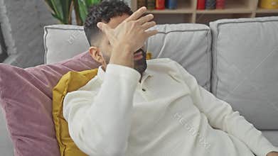 Surprise at home, smiling young hispanic man playfully covering eyes and face with hand, preserving blissful blindness