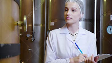 Winemaker woman checking and examining producing wine at winery in factory.