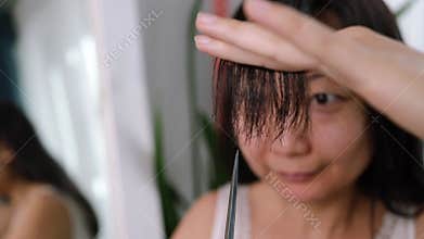 Young adult authentic asian woman self cutting bangs haircut with scissors.