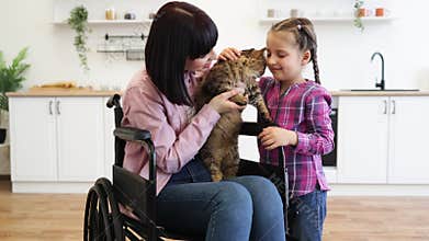 Mother in wheelchair with daughter and cat in cozy home