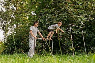 A father supports his child on playground equipment, fostering joy and exploration. Surrounded by lush greenery, they share a