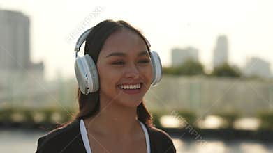 Portrait of happy Asian woman puts on over ear headphones on urban background