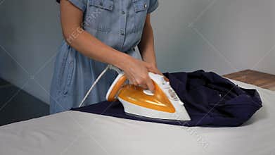 Unrecognizable woman ironing a man's shirt at home. Domestic life chore.