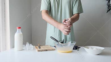 Man seasoning and whisking beaten eggs in glass bowl with pepper grinder in kitchen with milk during breakfast